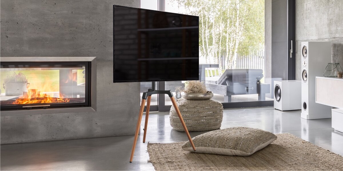 Stojak podłogowy HAMA do TV 32-65 cali 220873 Telewizor na stylowym stojaku tripod umieszczony w luksusowym salonie z kominkiem i dużym oknem tarasowym.