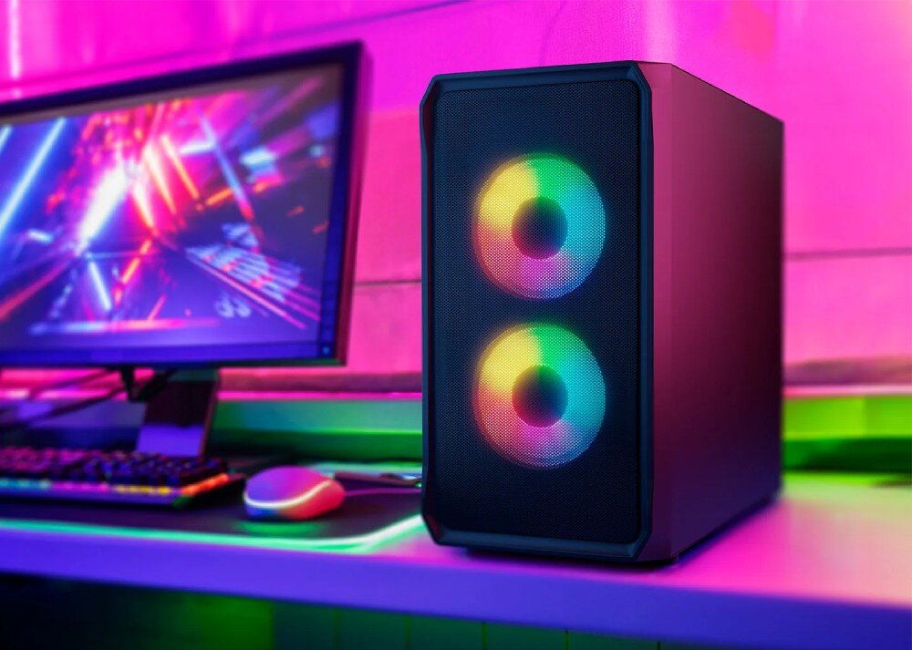 Komputer MAD DOG GeForce RTX5060 DLSS 4 Reflex Edition 2 LOGIC-A09WR32WP Komputer stacjonarny z podświetleniem ARGB stojący na biurku obok monitora, klawiatury i myszy, w tle różowe i fioletowe światła, opis