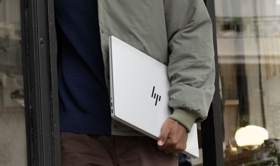 Mężczyzna w zielonej kurtce trzymający zamknięty laptop HP OmniBook w srebrnej obudowie, wychodząc z budynku, podkreślający mobilność i szybkość dzięki dyskowi SSD. - Dysk SSD PCIe Gen4 NVMe M.2 
