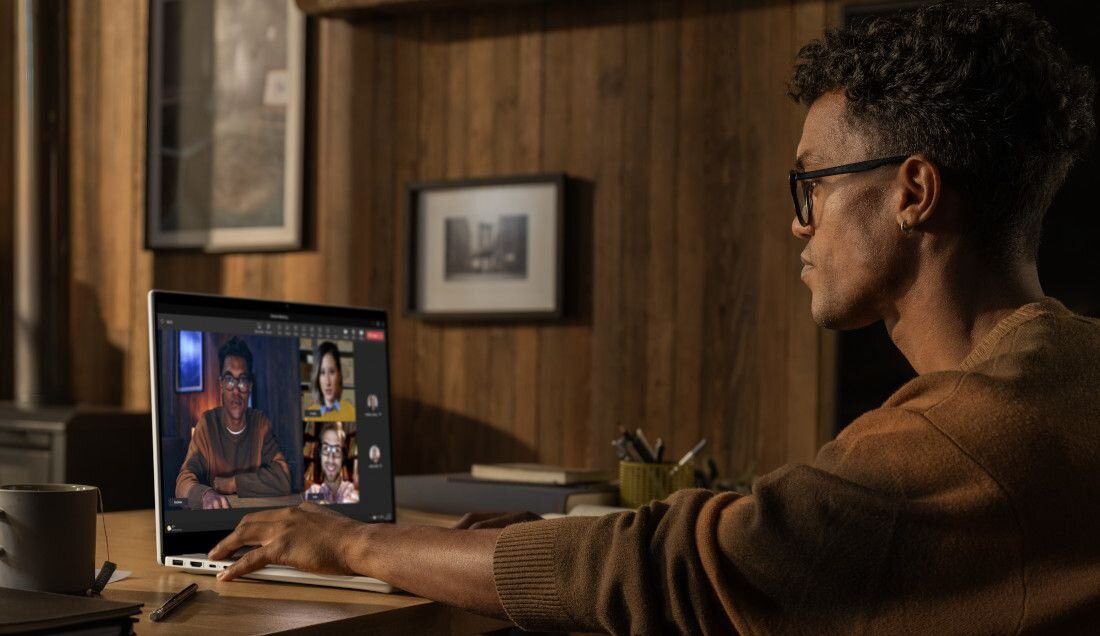 Mężczyzna w brązowym swetrze i okularach podczas wideokonferencji na laptopie HP OmniBook, na ekranie czterech uczestników, w tle domowe biuro, podkreślający funkcje AI do komunikacji. - HP AI Companion, Intel AI Boost  