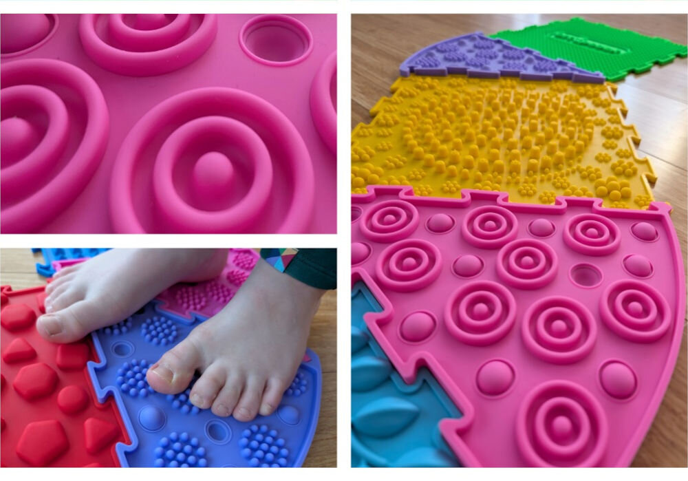 Mata sensoryczna ORTOPEDEK 910169 Zestaw mat (9 elementów) Wielokolorowy Zbliżenie na różową matę sensoryczną z wypustkami w kształcie koncentrycznych okręgów oraz bose stopy dziecka stojące na kolorowych puzzlach ortopedycznych.