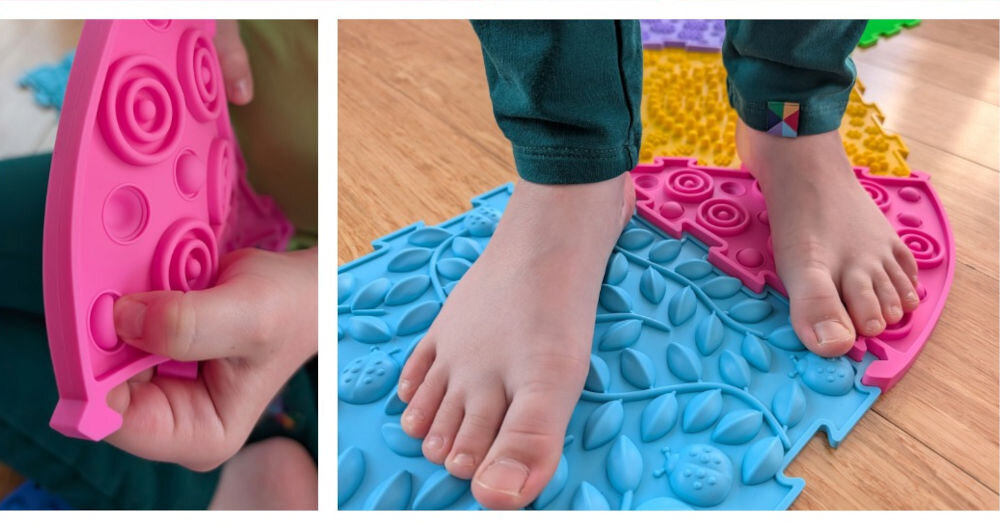 Mata sensoryczna ORTOPEDEK 910169 Zestaw mat (9 elementów) Wielokolorowy Dziecko testuje palcami elastyczność różowego elementu ścieżki sensorycznej oraz stoi boso na jasnoniebieskiej macie z wypukłym motywem liści i biedronek