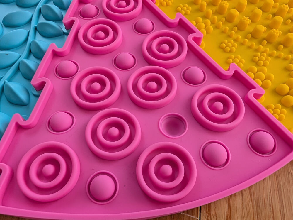 Mata sensoryczna ORTOPEDEK 910169 Zestaw mat (9 elementów) Wielokolorowy Detal różowej maty sensorycznej w kształcie trójkąta z wypukłymi pierścieniami i półkulami, ułożonej obok żółtego elementu z drobnymi wypustkami.