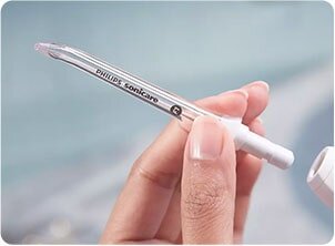 Osoba trzyma w dłoni przezroczystą końcówkę irygatora z widocznym napisem \'PHILIPS Sonicare\'.