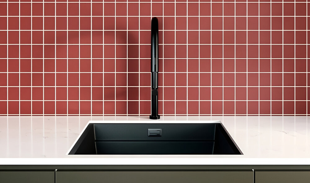 Czarna bateria kuchenna z wyciąganą wylewką zamontowana nad czarnym zlewem, na tle czerwonej ściany z białymi fugami.