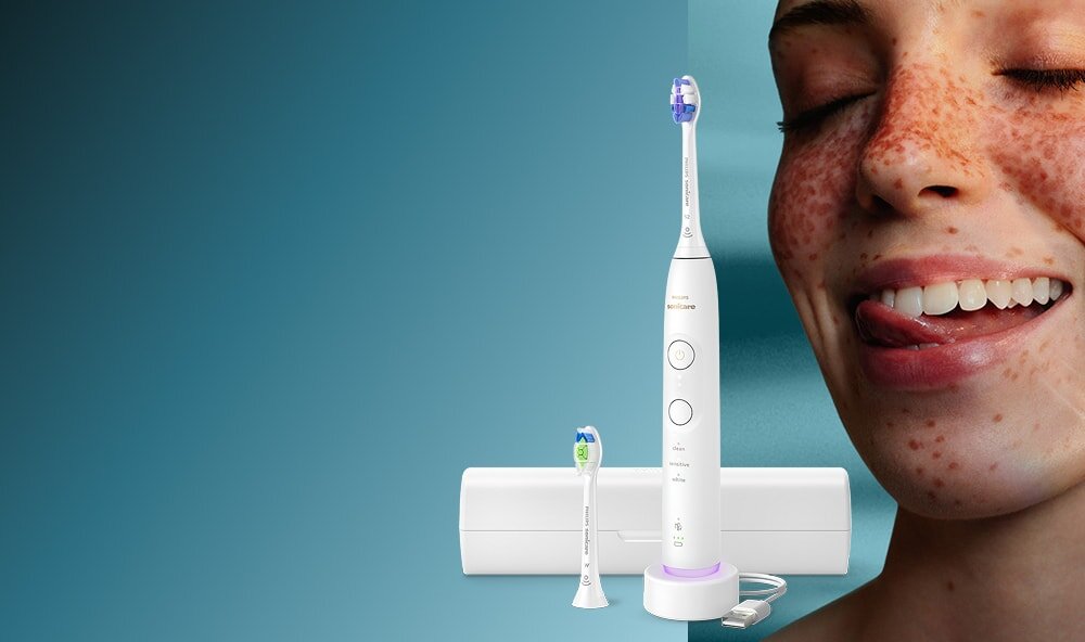 Zbliżenie na twarz uśmiechniętej kobiety, która językiem przesuwa po zębach. Obok szczoteczka soniczna z etui.