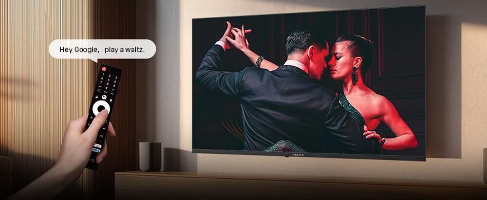 METZ 32MQF7030Z sterowanie głosem, Google Assistant, wygodne wyszukiwanie, telewizor zawieszony na ścianie, ręka trzymająca pilot