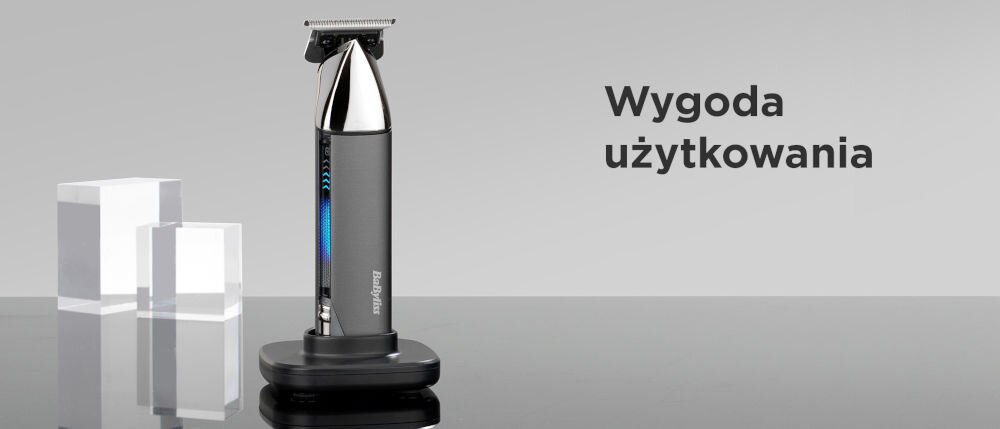 Na obrazie widoczny jest trymer stojący na podstawce, obok dwóch przezroczystych sześcianów. Po prawej stronie znajduje się tekst: \'Wygoda użytkowania\'.