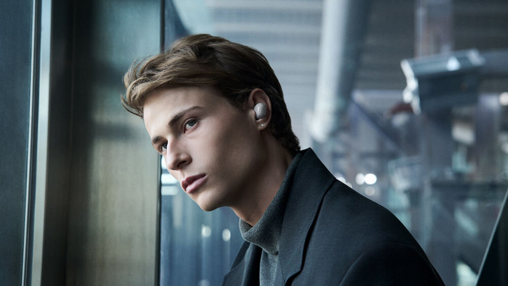 Słuchawki dokanałowe SONY WF-1000XM6 ANC Zbliżenie na profil mężczyzny przy oknie, eksponujące minimalistyczny design srebrnej słuchawki Sony WF-1000XM6.