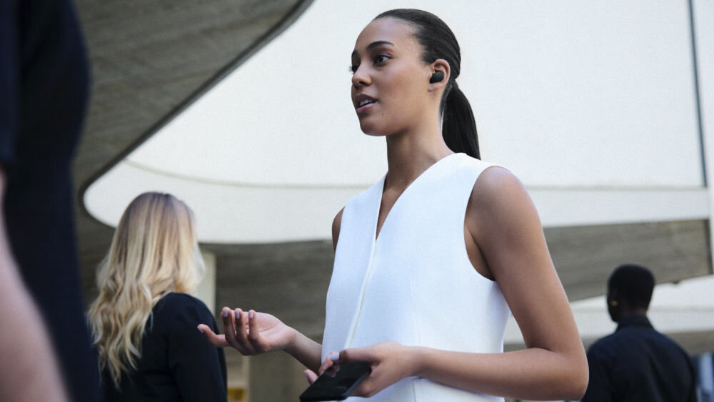 Słuchawki dokanałowe SONY WF-1000XM6 ANC Kobieta rozmawiająca przez telefon w czarnych słuchawkach dousznych Sony WF-1000XM6 w miejskim otoczeniu.