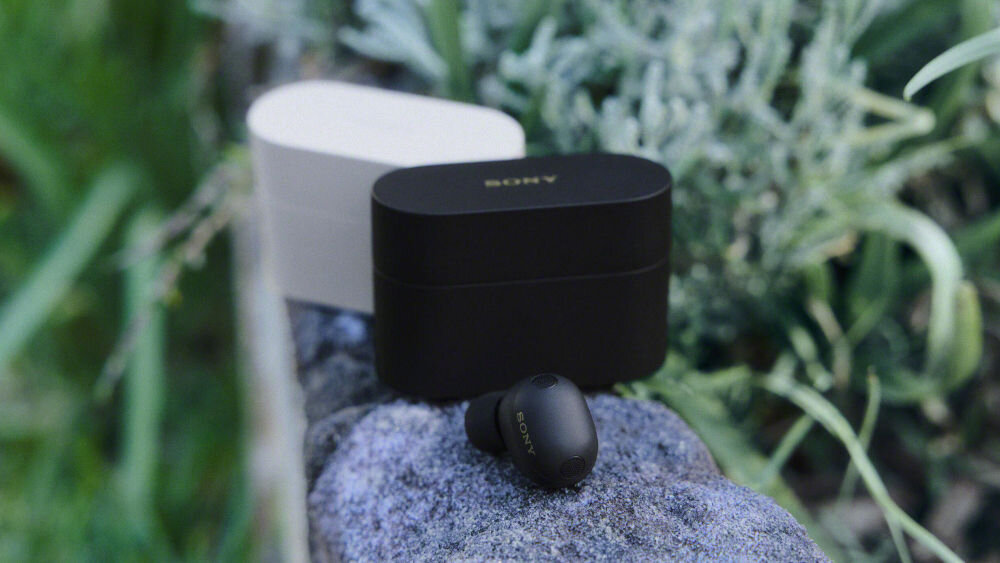 Słuchawki dokanałowe SONY WF-1000XM6 ANC Czarne i beżowe etui ładujące oraz czarna słuchawka Sony WF-1000XM6 na kamieniu w otoczeniu zieleni.