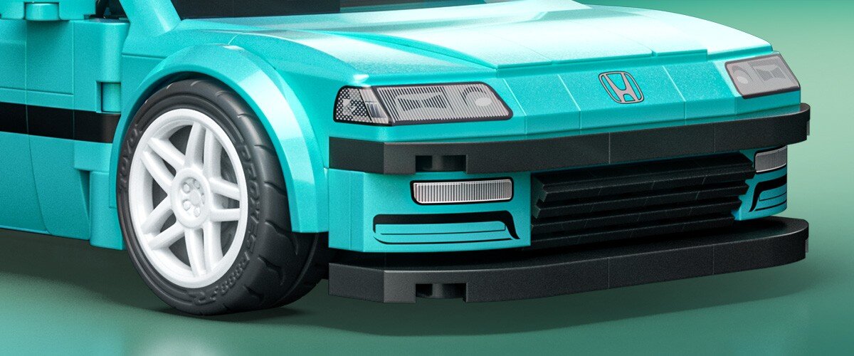 Zbliżenie na przód turkusowego modelu samochodu z klocków, z widocznym logo Honda na masce. Samochód ma białe felgi i czarne detale na zderzaku.