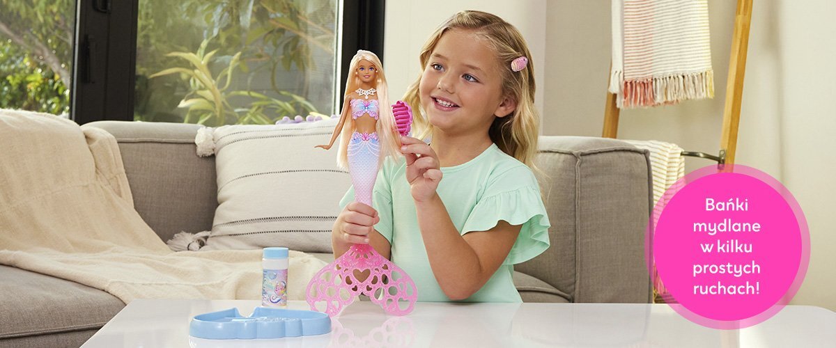 Dziewczynka bawiąca się lalką Barbie przy stole, obok widnieje napis 'Bańki mydlane w kilku prostych ruchach!'.