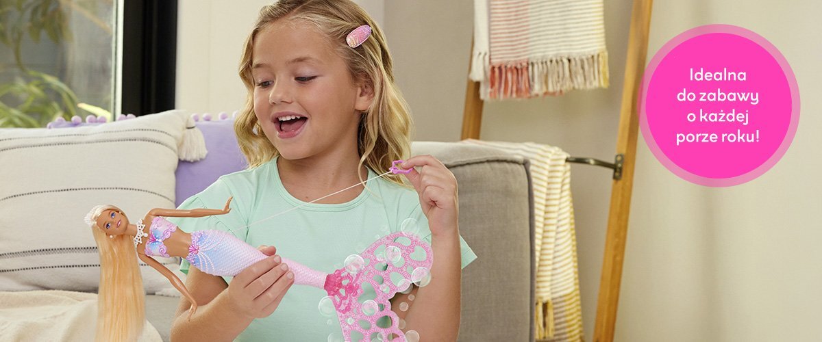 Dziewczynka bawiąca się lalką Barbie w salonie, obok widnieje napis 'Idealna do zabawy o każdej porze roku!'.