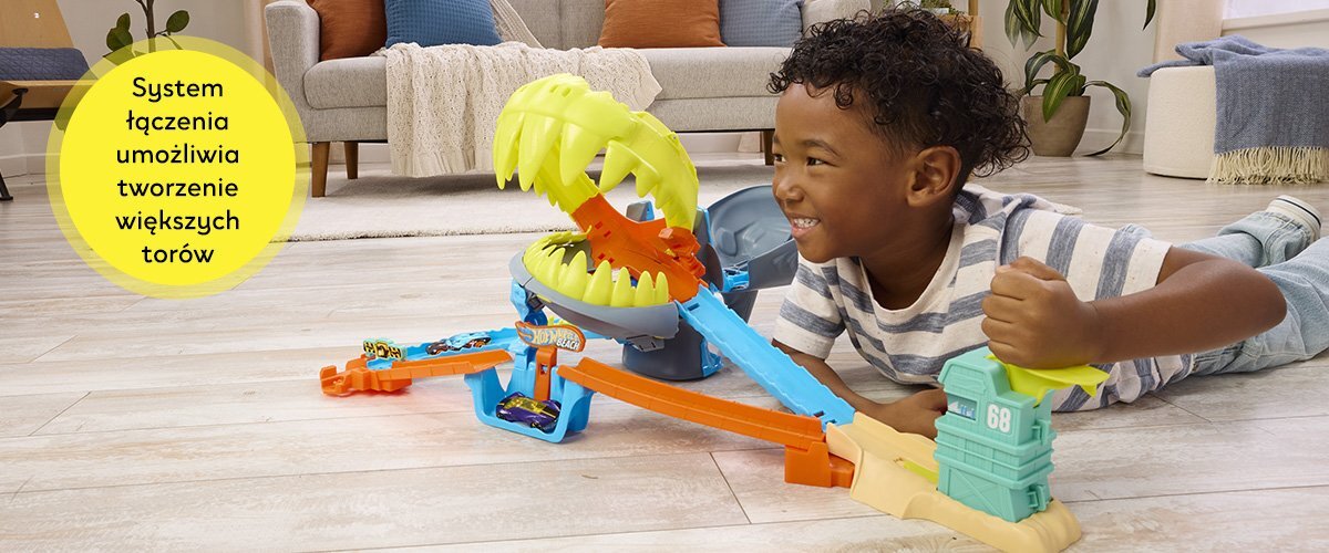 Dziecko bawi się torem Hot Wheels z dużą paszczą rekina. Na żółtym tle widnieje tekst: \'System łączenia umożliwia tworzenie większych torów\'.