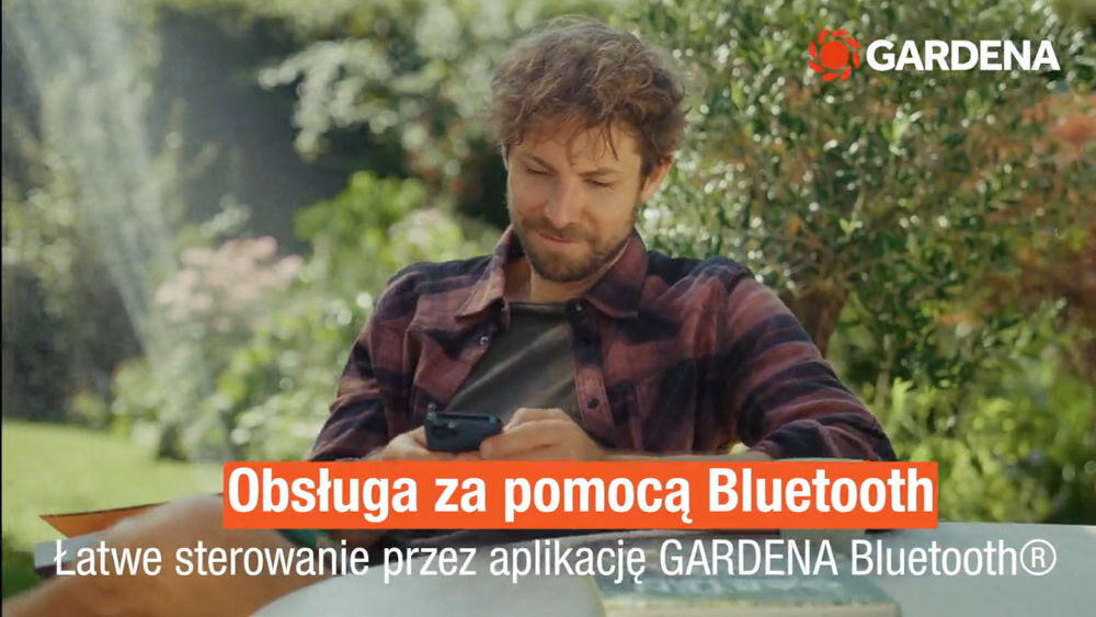 Osoba siedzi na zewnątrz, trzymając smartfon. Na obrazie widoczny jest tekst: \'Obsługa za pomocą Bluetooth Łatwe sterowanie przez aplikację GARDENA Bluetooth®\', a w rogu logo GARDENA.
