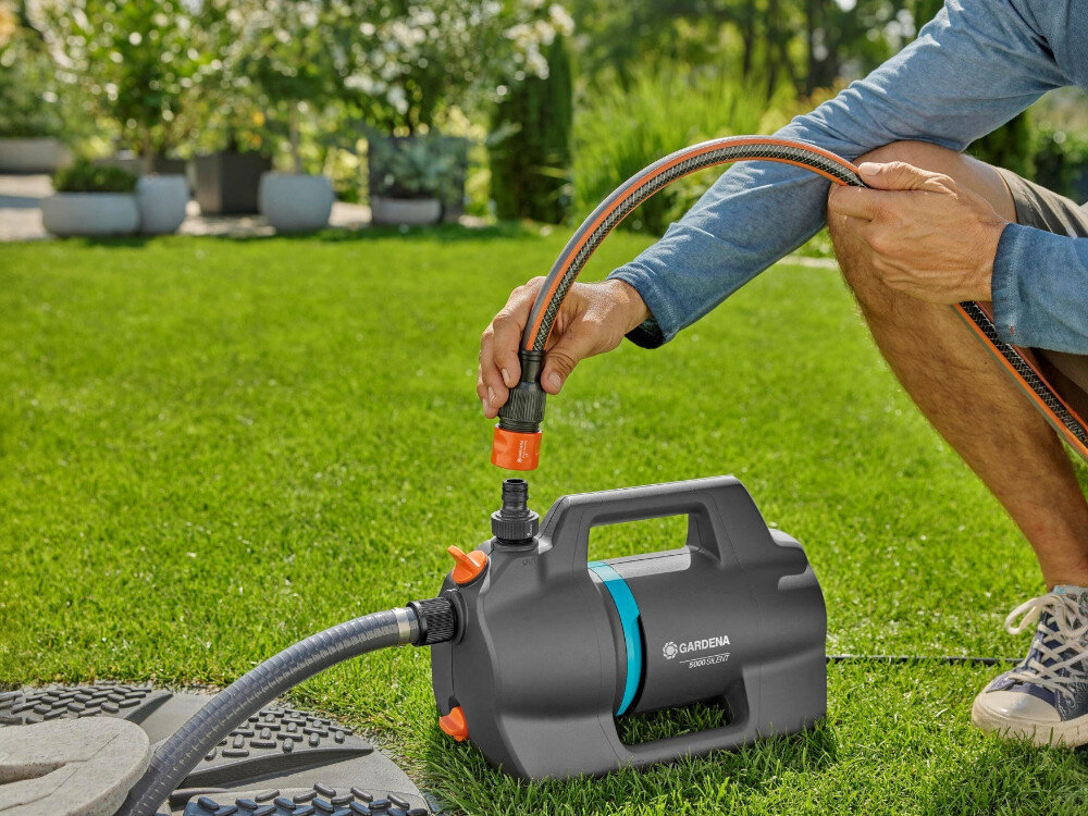 Pompa do wody GARDENA 09086-20 elektryczna, moc, woda, ciśnienie, bar, osoba wpina do pompy wąż na szybkozłączkę, w tle ogród