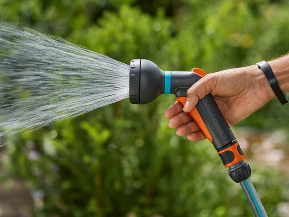 Pistolet zraszający GARDENA Classic 18367-20, impulsowy, automatyczny, ergonomiczny, wieczorny, dłoń trzyma pistolet podłączony do wody, w tle ogród