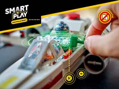 Na zdjęciu widać model statku kosmicznego z serii LEGO Star Wars z figurką robota w kokpicie. W lewym górnym rogu znajduje się logo \'SMART PLAY\' z napisem \'Revolution in Motion\'.