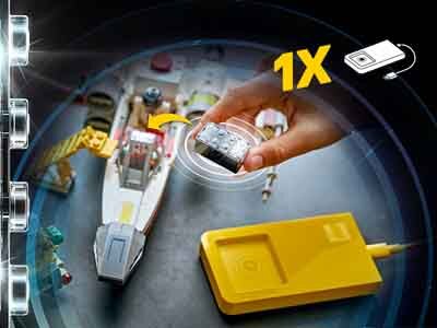 Na obrazie widoczny jest model statku kosmicznego z klocków LEGO oraz ręka trzymająca mały element. Obok znajduje się żółte urządzenie z kablem, a w rogu widnieje symbol z napisem \'1X\'.