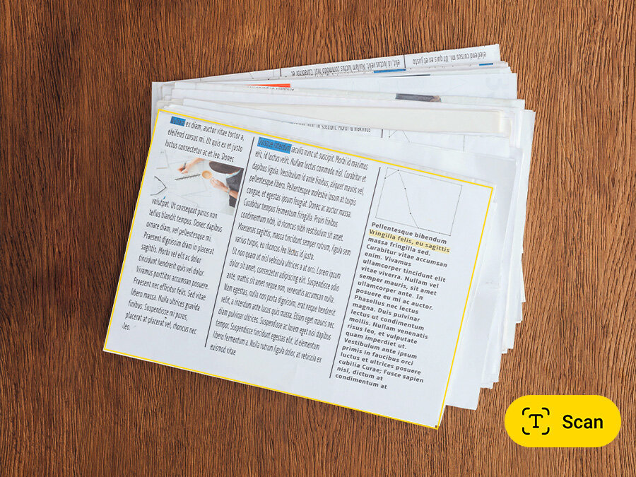 Widok z aparatu z funkcją skanowania pokazuje plik papierów ułożonych jeden na drugim na drewnianym stole. Ikona przycisku skanowania znajduje się w prawym dolnym rogu, na żółtym owalnym tle.