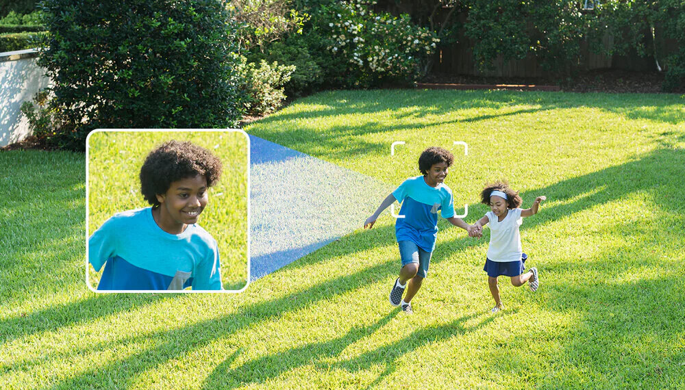 Dwoje dzieci biega po trawniku w słoneczny dzień. Na obrazie widoczny jest także powiększony fragment twarzy jednego z dzieci, co sugeruje funkcję śledzenia lub powiększania obrazu.