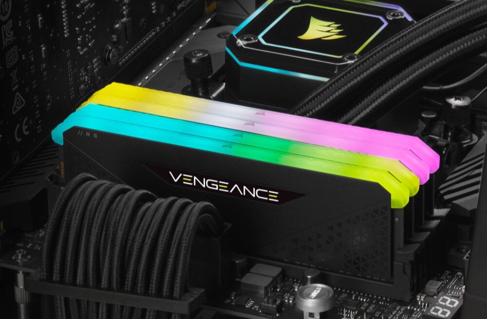 Komputer MAD DOG CORSAIR3500X-I02DR32 Zbliżenie na moduły pamięci RAM z napisem 'VENGEANCE' zamontowane na płycie głównej, z wielokolorowym podświetleniem na górnej krawędzi, w otoczeniu innych podzespołów komputera, pamięć, taktowanie, opóźnienia, podświetlenie