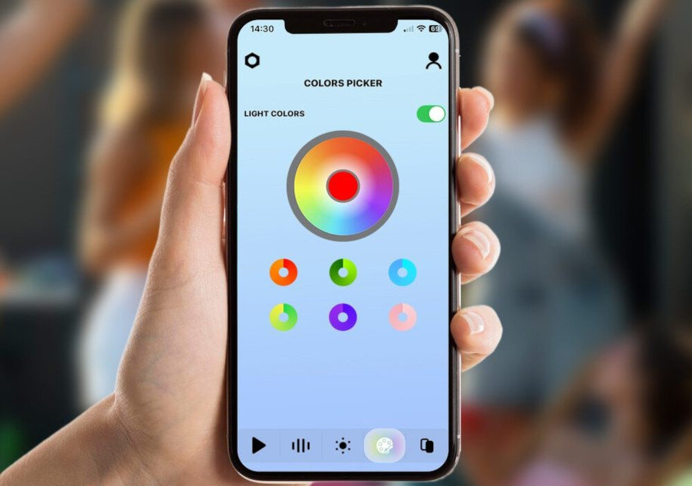 Osoba trzyma smartfon z aplikacją \'COLORS PICKER\' na ekranie, pokazującą koło kolorów i różne opcje wyboru barw. W tle widoczne są rozmyte sylwetki ludzi.