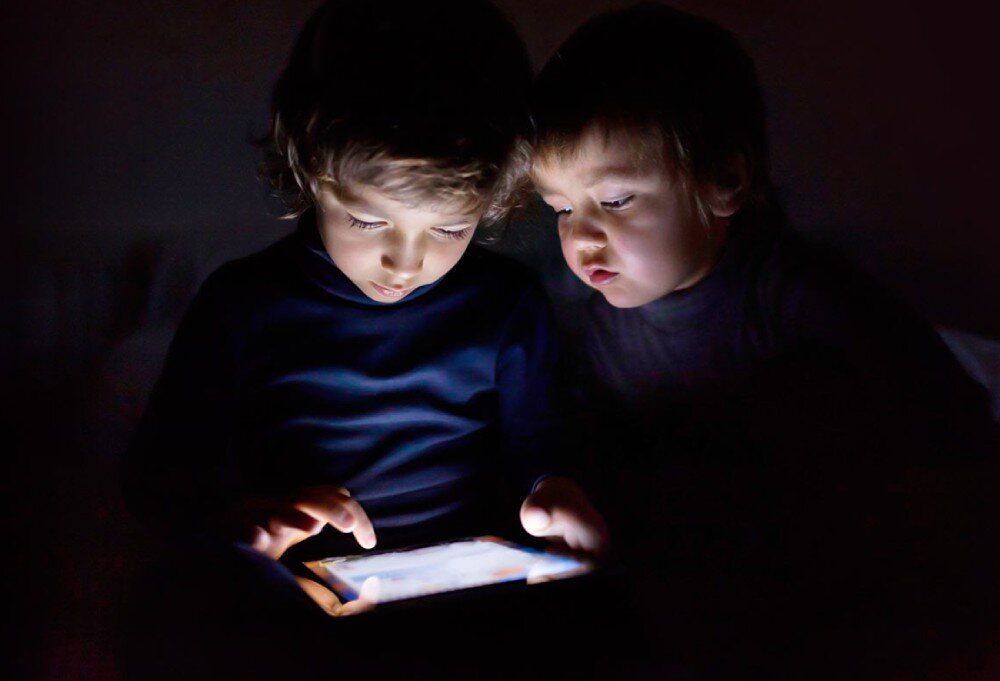 Router MERCUSYS AC12 Dwoje małych dzieci w ciemnym pomieszczeniu, patrzących z zainteresowaniem na ekran świecącego tabletu, zabezpieczenia, funkcje, szyfrowanie, kontrola rodzicielska