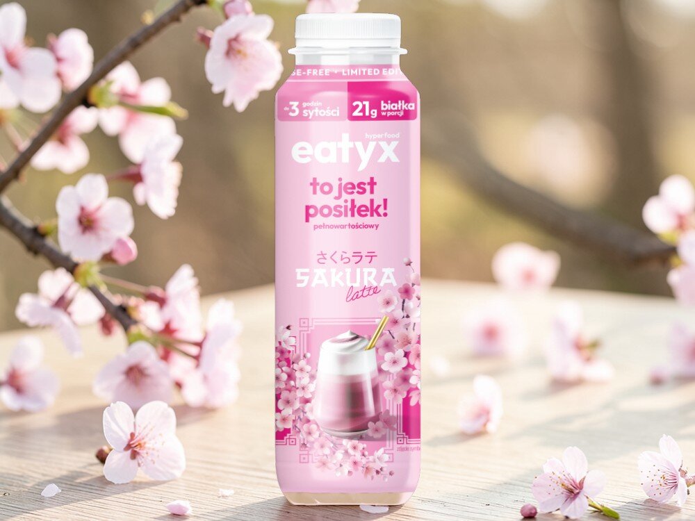 Posiłek w płynie EATYX Hyperfood Sakura Latte (300 ml) jasne tło drewniana podłoga butelka stoi na podłodze wokół butelki różowe kwiatki wiśni wanilii 22 witamin i minerałów biotyna (10,2 µg) witamina B12 (0,8 µg) chrom (6,6 µg) selen (9,3 µg) witamin E (5,4 mg) wapń (540 mg) wspierają zdrowie skóry, włosów, paznokci i metabolizmu energetycznego