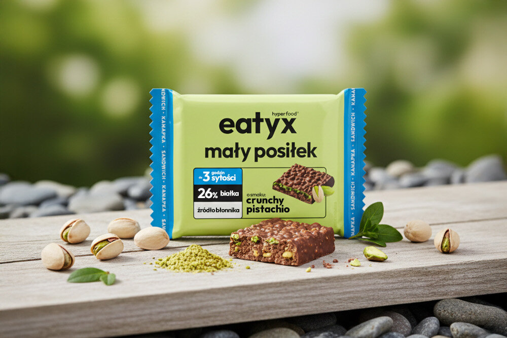 Baton proteinowy EATYX Hyperfood Pistacjowy (8 x 50 g) jasnozielone tło drewniany blat baton wokół pistacje mały posiłek nie wymaga przygotowania ani podgrzewania 8 batonów