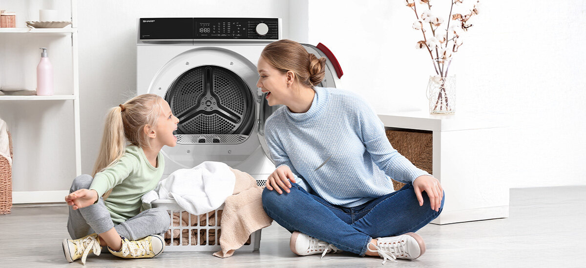 SUSZARKA SHARP KD-NHL8S9GWC-PL Suszarka stoi w jasnym wnętrzu, a obok niej siedzą kobieta i dziecko zajmujące się praniem. Scena pokazuje domowe, spokojne otoczenie i wygodne korzystanie ze sprzętu system wykrywania awarii Child Lock blokada rodzicielska bezpieczne użytkowanie kontrola pracy
