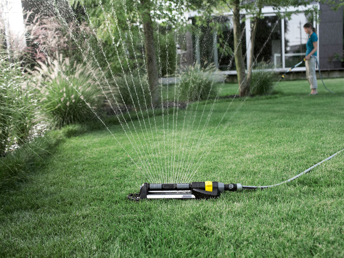 Zraszacz KARCHER OS 5.320 S, szybkozłącza, system, ogród, woda, w tle ogród i dom, na pierwym planie zraszacz podlewa trawnik
