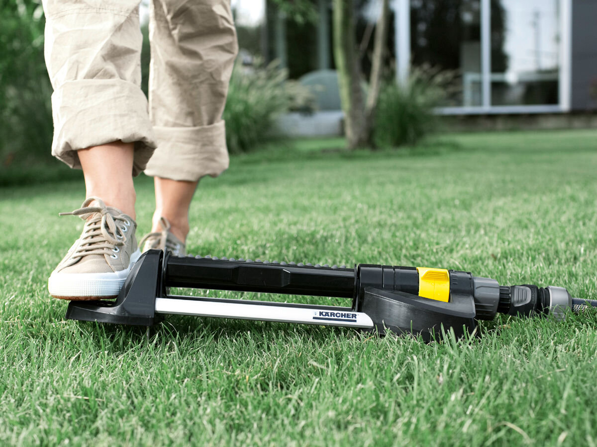 Zraszacz KARCHER OS 5.320 S, zawieszenia, ucho, konstrukcja, Przechowywanie, w tle dom, na pierwszym planie osoba dociska ucho zraszacza do trawnika