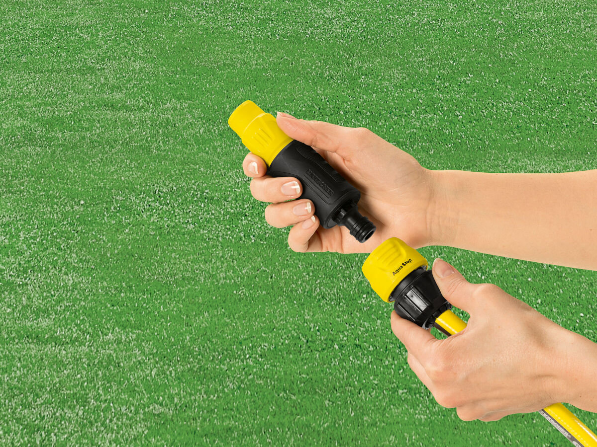 Wąż ogrodowy KARCHER PrimoFlex 1/2 50 m 2.645-139.0, odporność, uszkodzenia, pogoda, warunki, w tle trawnik, na pierwszym planie wąż z rozpylaczem trzymany w dłoniach