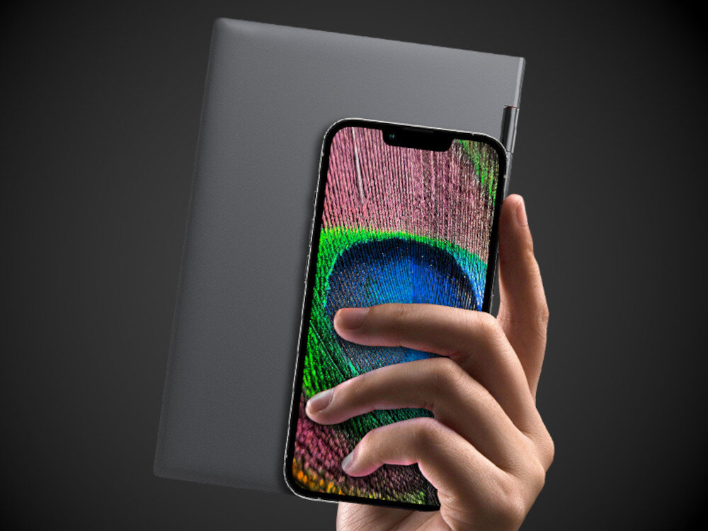 Osoba trzyma smartfon z kolorowym wyświetlaczem przedstawiającym wzór przypominający pióro pawia. W tle widoczny jest szary laptop z zamkniętą pokrywą.