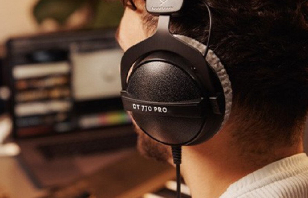 Słuchawki nauszne BEYERDYNAMIC DT 770 Pro 32 Ohm dynamiczne przetworniki reakcja impulsowa, osoba z założonymi słuchawkami nausznymi siedząca przed laptopem