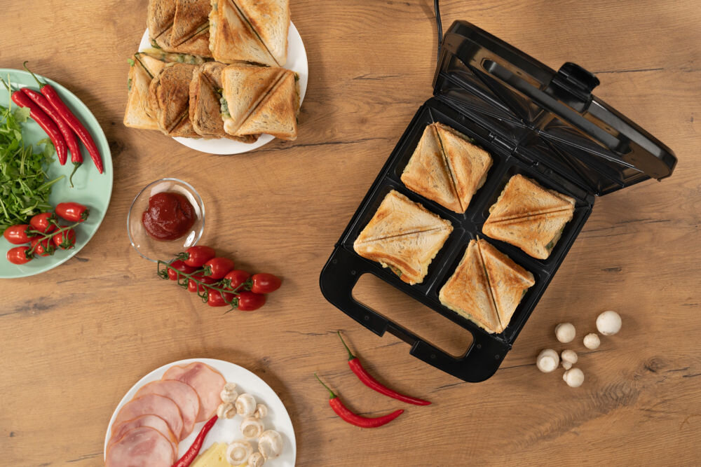 Opiekacz GOTZE & JENSEN SM703X widok z góry na otwarty opiekacz stojący na drewnianym bralcie obok talerz z kanapkami i warzywa