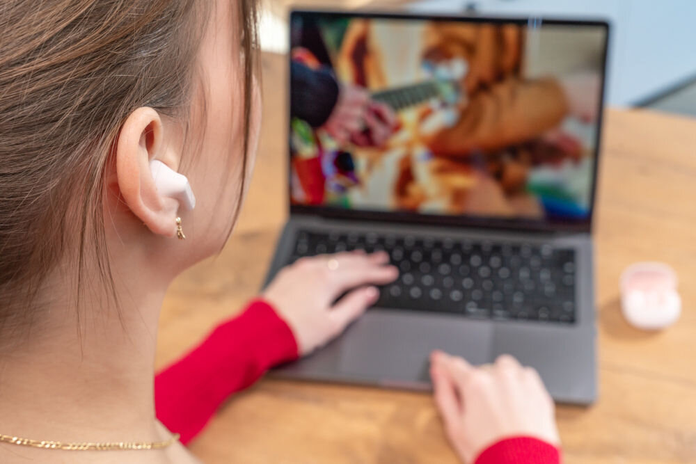 Słuchawki douszne XMUSIC XTW300P różowy Ujęcie z bliska na ucho kobiety, w którym znajduje się rożowa słuchawka douszna z pałąkiem.