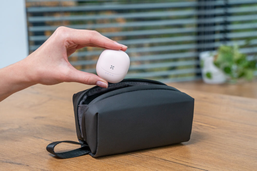 Słuchawki douszne XMUSIC XTW300P różowy Dłoń trzyma zamknięte, czarne etui do słuchawek z widocznym logo i diodami, unosząc je nad otwartym, czarnym pokrowcem materiałowym (saszetką).