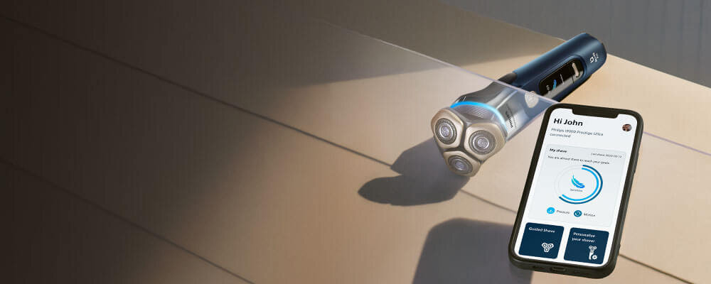 Oparty o ręcznik smartfon z włączoną aplikacją na monitorze. Obok golarka ze świecącym niebieskim ringiem. 