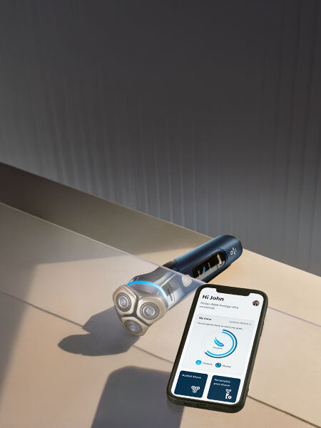 Oparty o ręcznik smartfon z włączoną aplikacją na monitorze. Obok golarka ze świecącym niebieskim ringiem. 