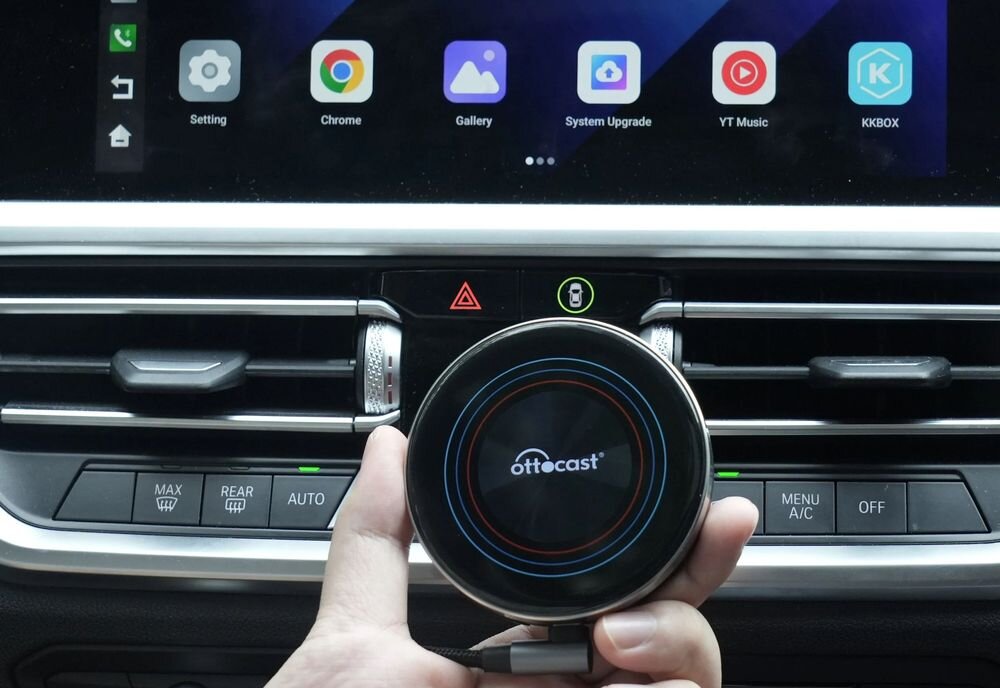OTTOCAST OttoAibox i3 bezprzewodowy CarPlay i Android 12 komfort jazdy bez kabli, osoba trzsymająca adapter w reku na tle kokpitu