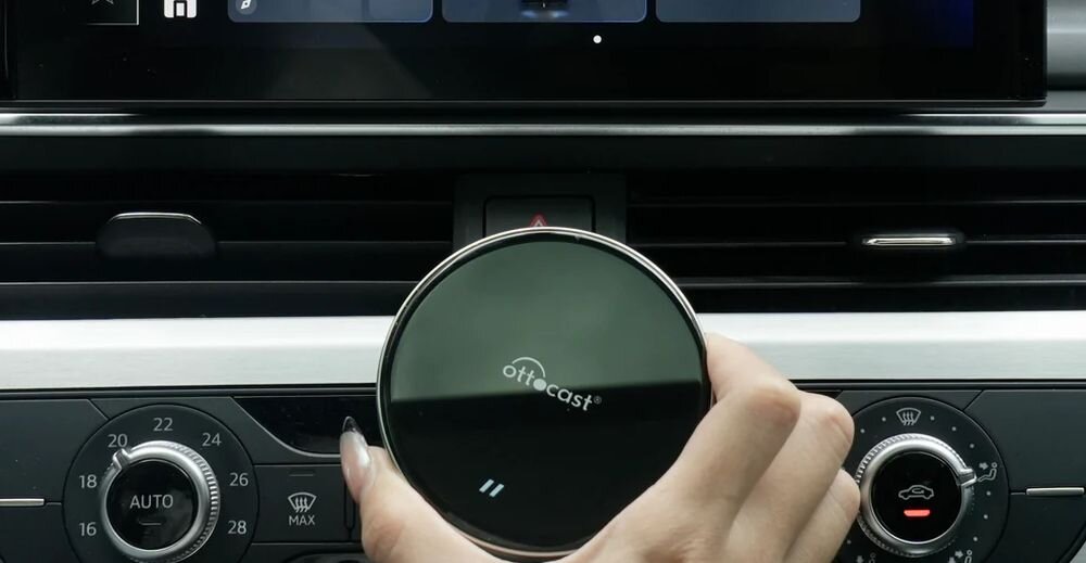 Adapter OTTOCAST OttoAibox P3 Lite Wi-Fi 5 Dual-Band 2.4 GHz 5.1 GHz Nano SIM 2G 3G 4G karta TF do 256 GB, osoba trzymająca adapter w ręku na tle kokpitu samochodu