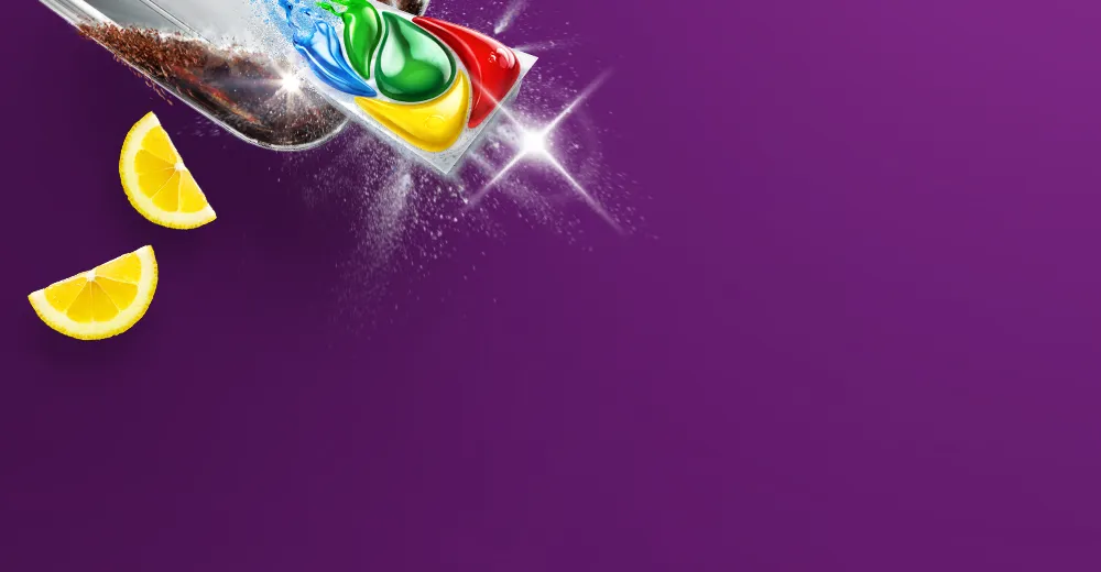 Kolorowa kapsułka Fairy na częściowo zabrudzonej tłuszczem blaszce z kawałkami cytryn i ikonami funkcji produktu.