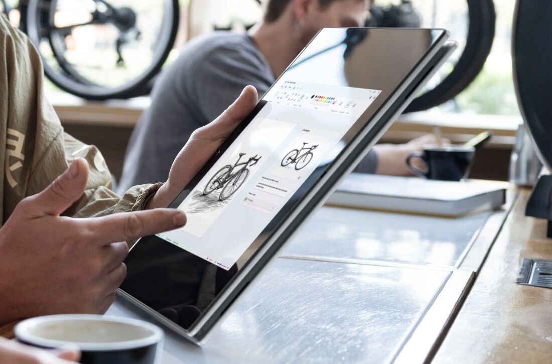 Laptop HP OmniBook wykorzystywany do pracy kreatywnej z rysunkiem roweru na ekranie dotykowym w kawiarni.