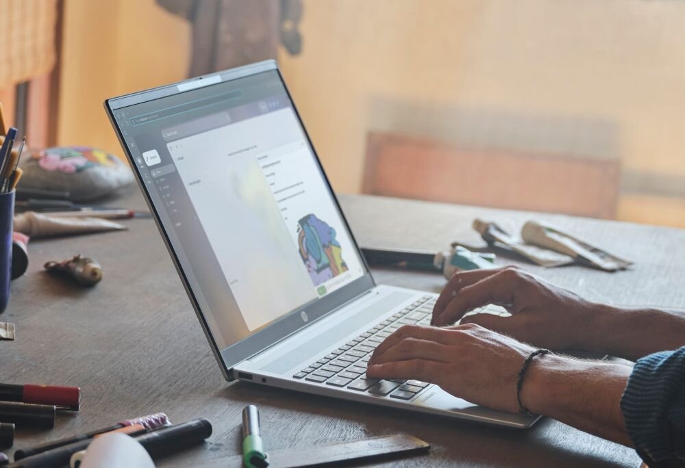 Ręce mężczyzny piszące na laptopie HP OmniBook 5 16-BC1 z otwartym programem graficznym na drewnianym biurku z markerami - Ogólny opis serii OmniBook 5 16-BC1