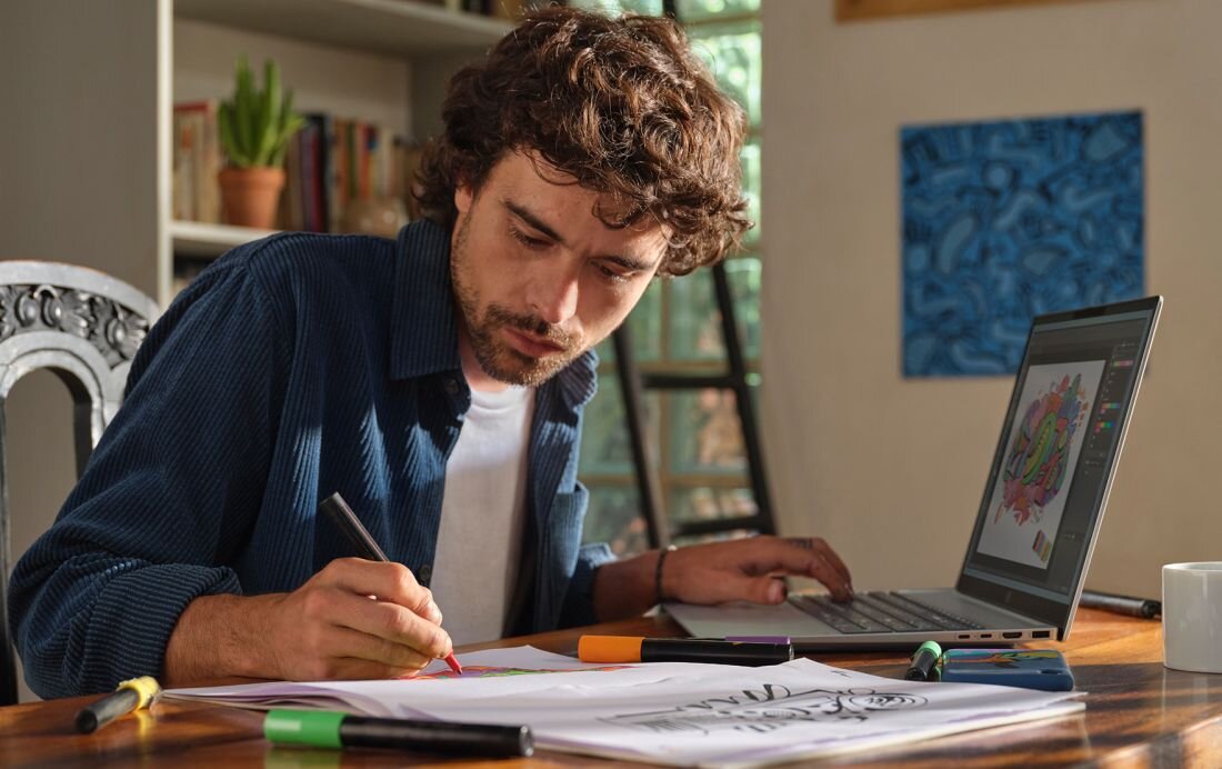 Mężczyzna w niebieskiej koszuli w paski rysujący na papierze obok laptopa HP OmniBook 5 16-BC1 - Wi-Fi 6E, Bluetooth 5.3