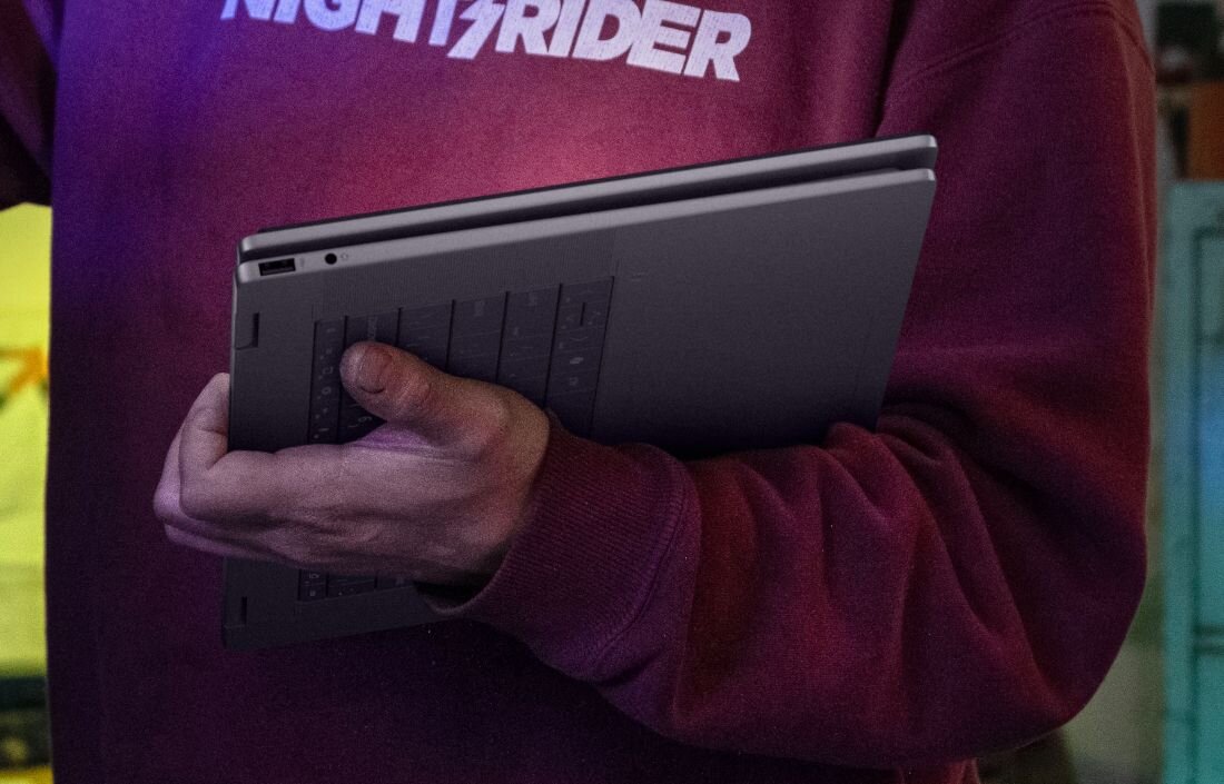 Trzymanie zamkniętego laptopa HP OmniBook z certyfikatem ENERGY STAR, bordowa bluza z napisem Nightrider.