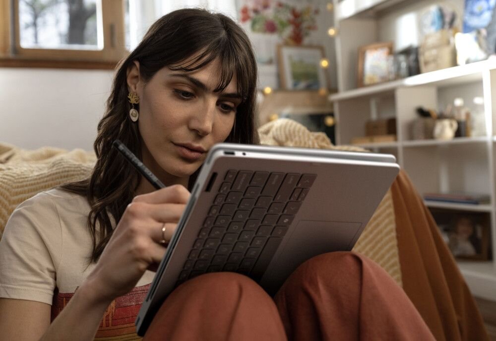 Laptop HP OmniBook w srebrnej obudowie z ekranem prezentującym kolorową abstrakcyjną tapetę w odcieniach niebieskiego, różowego i pomarańczowego z płynącymi kształtami, widok z góry na klawiaturę i touchpad, podkreślający wydajność pamięci LPDDR5. - Pamięć LPDDR5   